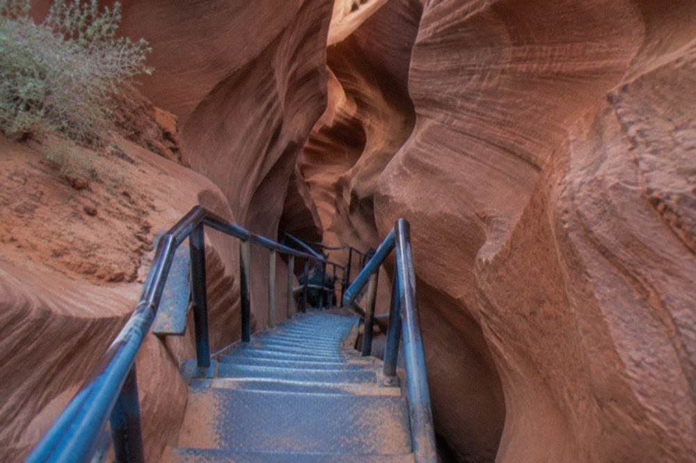A metal staircase descending into a narrow sandstone slot canyon passage