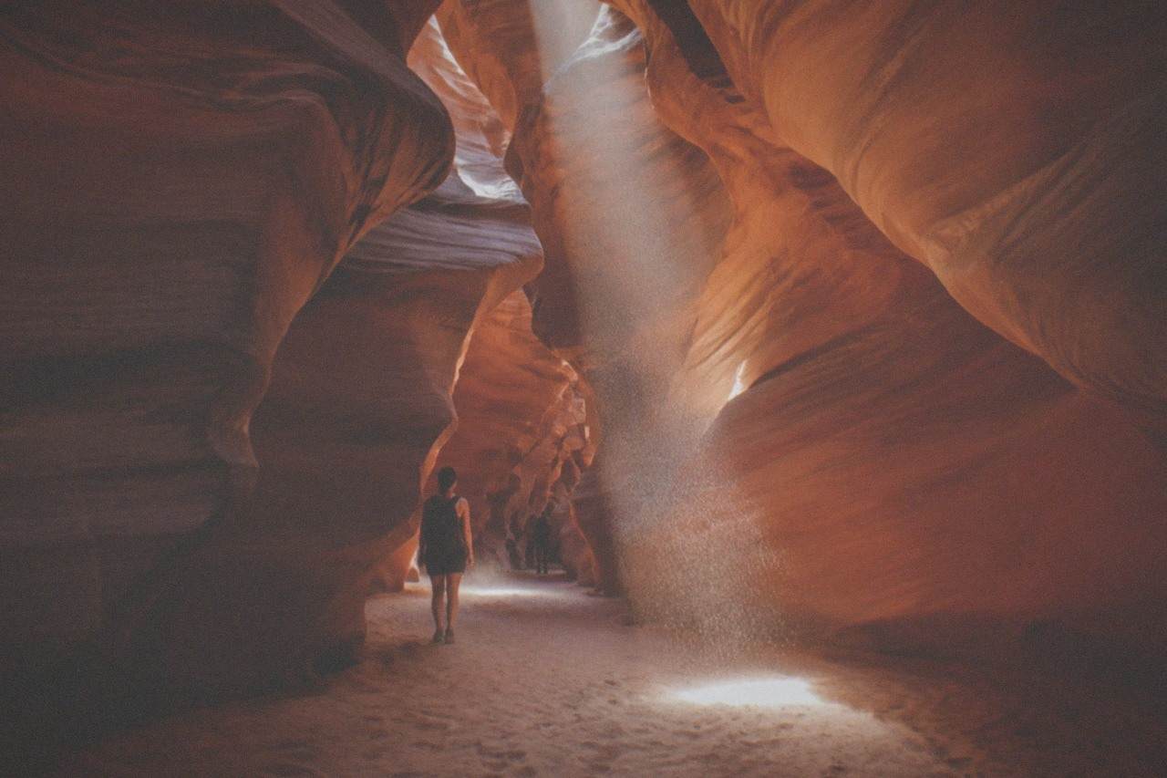 Narrow swirling sandstone walls of a slot canyon lit by a shaft of daylight