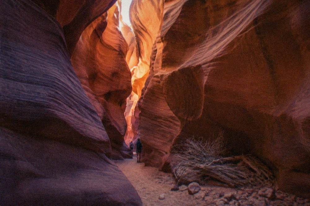 A narrow slot canyon corridor with layered orange and red sandstone walls under a thin strip of sky