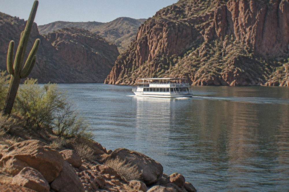 A Dolly Steamboat vessel gliding across calm Canyon Lake with red rock cliffs on both sides.