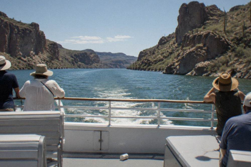 A tour boat moving across a desert lake with canyon walls rising on both sides
