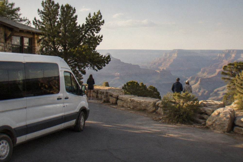 Tour van parked at a Grand Canyon South Rim overlook with the canyon stretching to the horizon