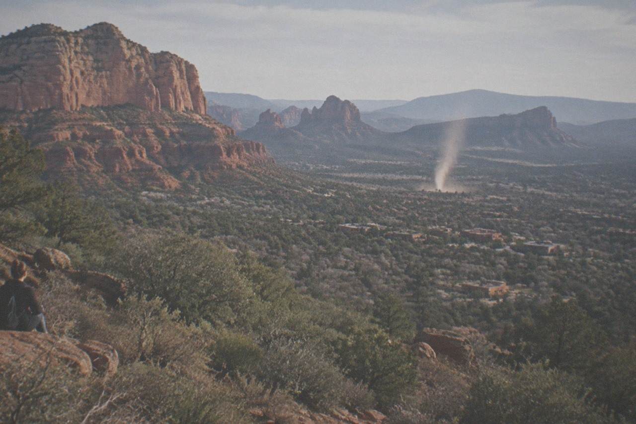 Red rock cliffs rising above a desert valley with scrub and distant mountains under a clear sky