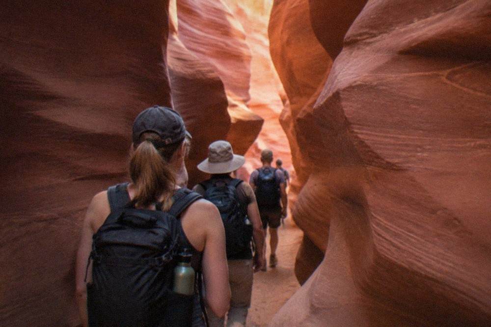 A guided tour group walking single file through a narrow sandstone slot canyon with warm light on the curved walls