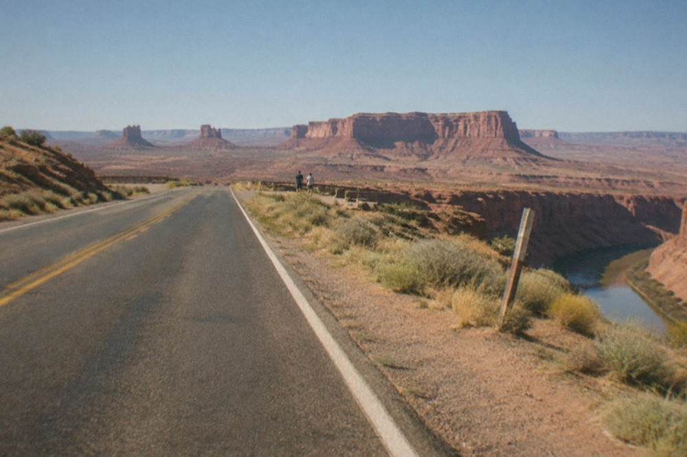 A desert highway stretching toward red rock mesas under a wide blue sky