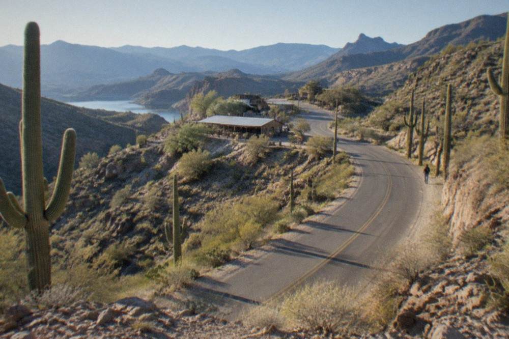 A narrow desert road curving between rocky hills with saguaro cacti