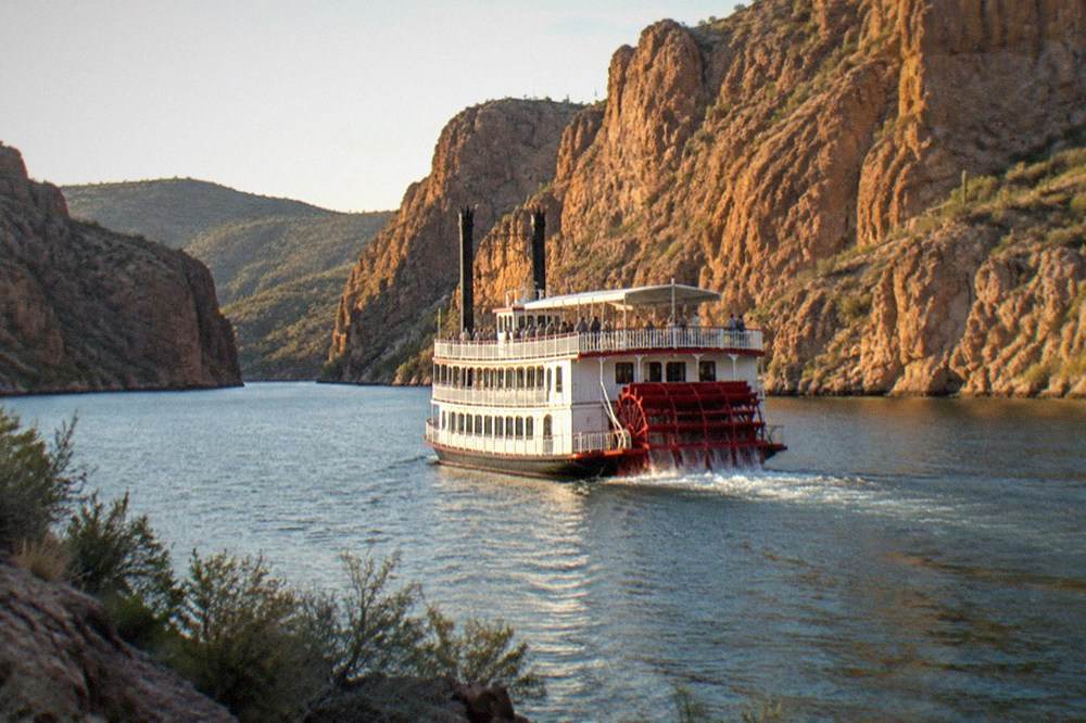 A paddlewheel steamboat cruising between steep rocky canyon walls on a lake