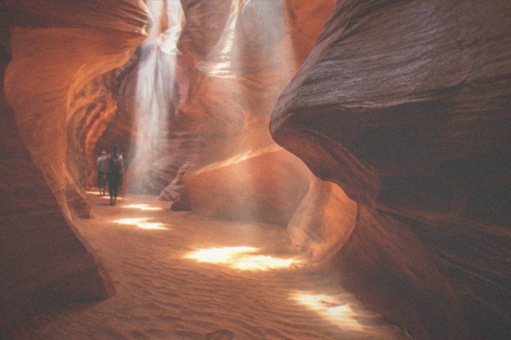 Shafts of sunlight cutting through dust inside a sandstone slot canyon
