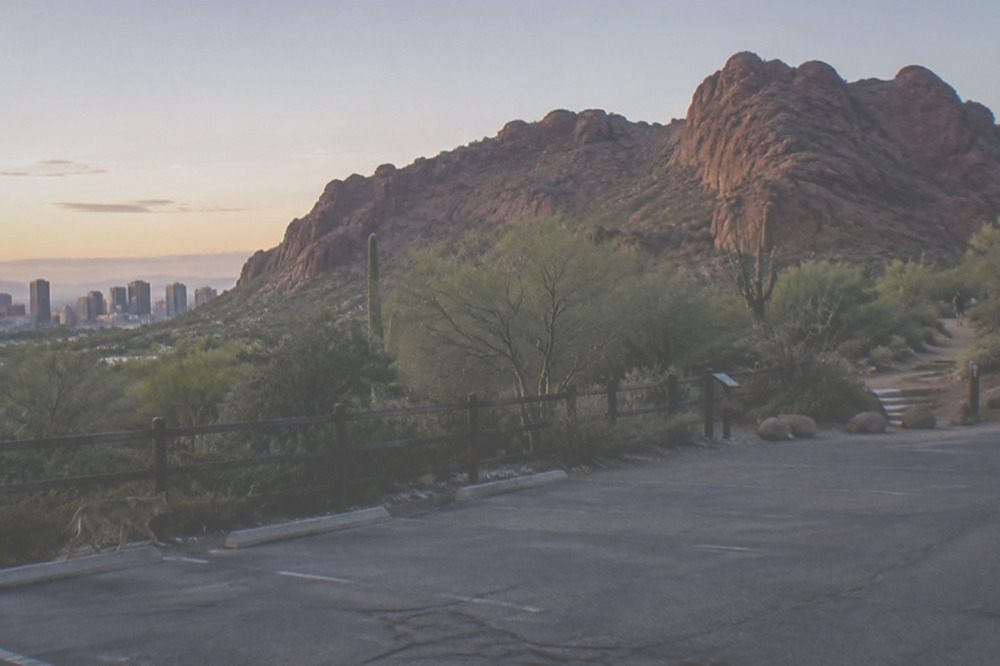 A small trailhead parking lot with red rock slopes rising behind it in early light
