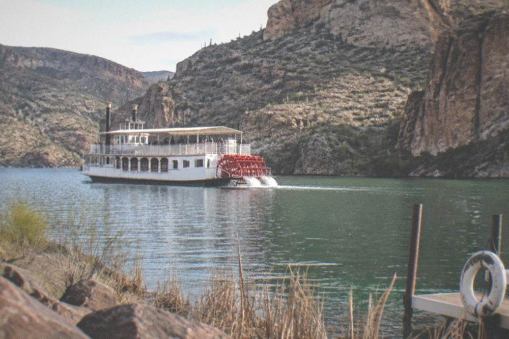 A steamboat cruising on a desert lake framed by rocky canyon walls