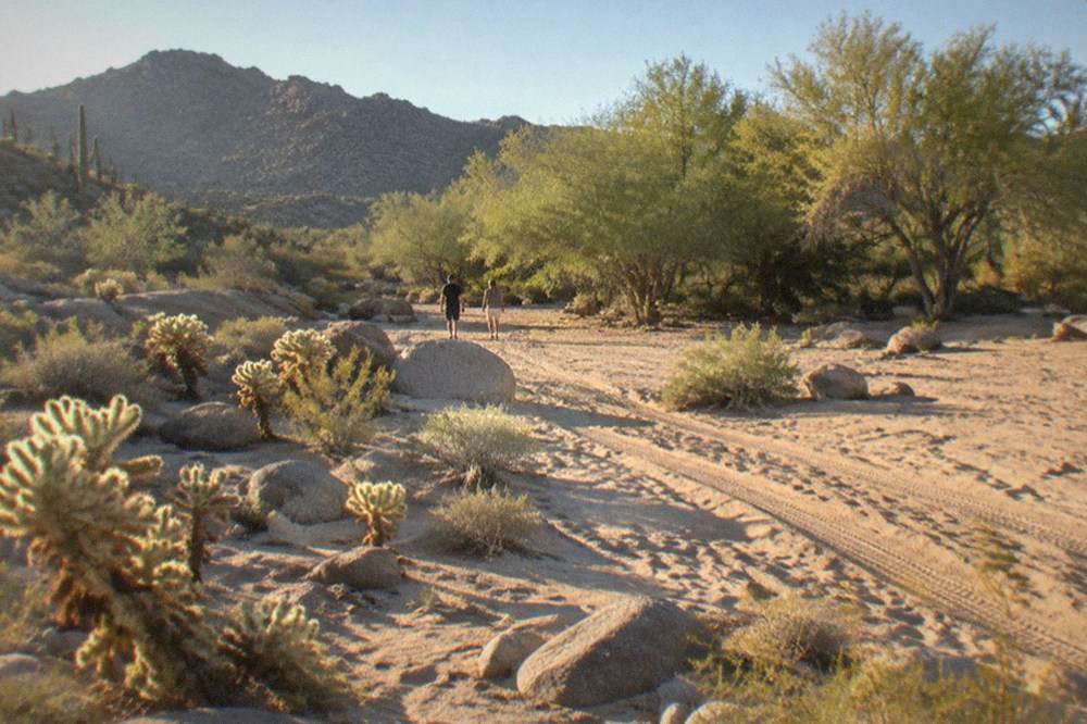 An open desert trail crossing sandy washes between granite boulders and cactus