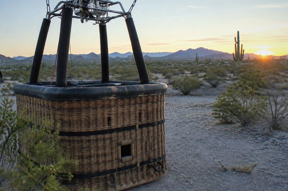 A balloon basket upright on a flat desert landing field with chase vehicle in the distance