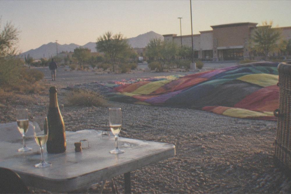 A small table set with champagne glasses on a desert landing field beside a deflating balloon