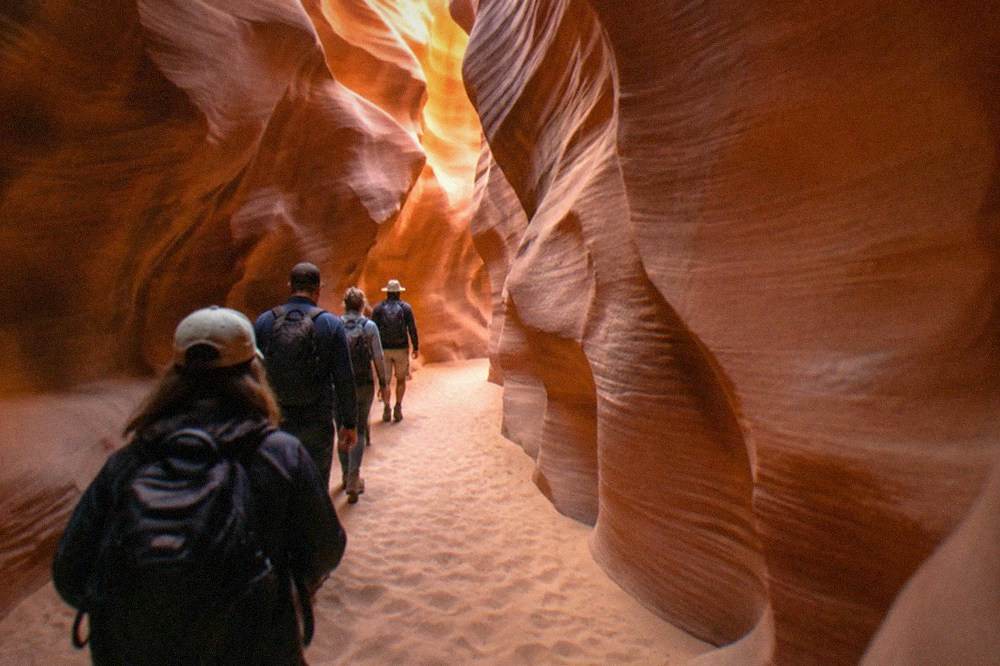 A guided group walking through the sandy floor of a narrow slot canyon
