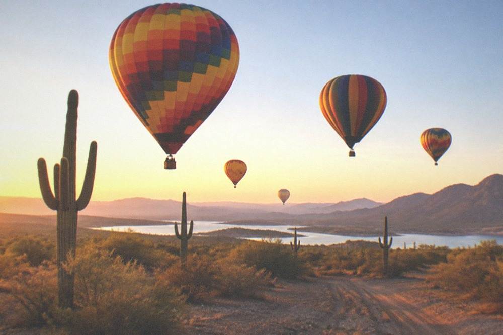 Several hot air balloons floating low over open desert at sunrise