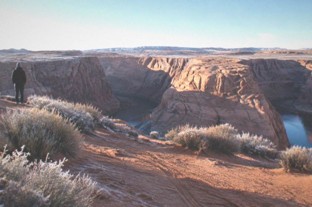 Sunlit sandstone walls above a stretch of open desert near a lake shoreline