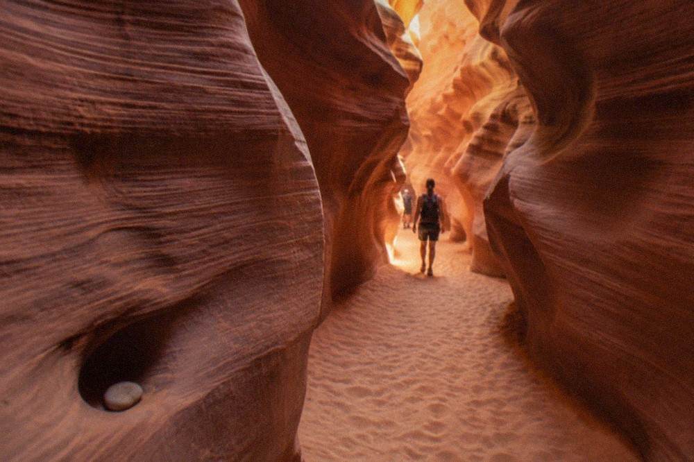 A narrow slot canyon passage with smooth curved sandstone walls lit in warm orange tones