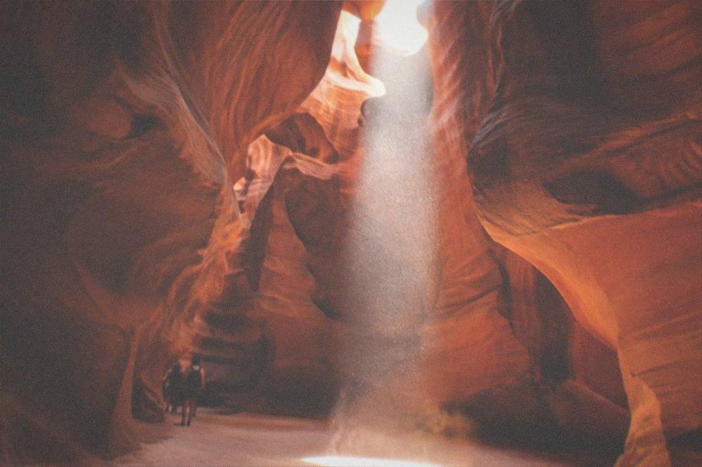 Sunlight falling through a gap in slot canyon sandstone onto the sandy floor