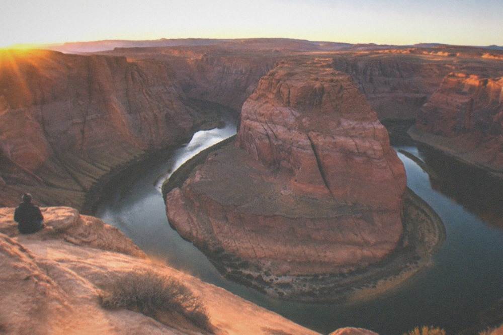 A sweeping bend in a river below tall orange sandstone cliffs under a clear sky