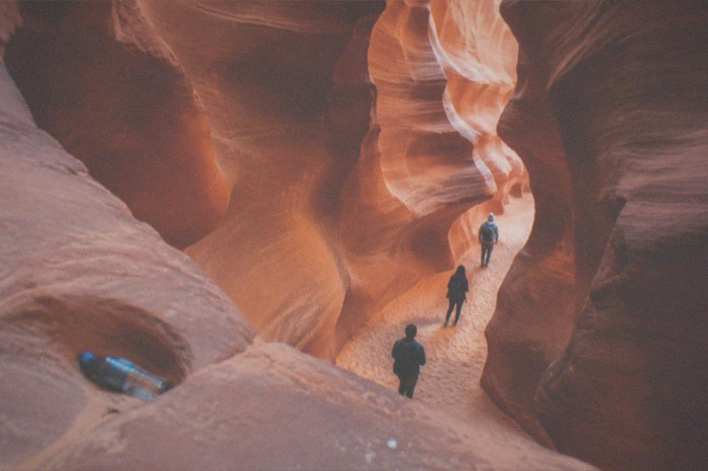 A narrow sandstone slot canyon with light beams reaching a sandy floor